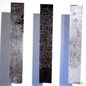 Canon by Heather Page is a trio of 60” by 11” encaustic artworks on paper of calligraphic text scraped into or from a black waxy layer covering a silver ground
