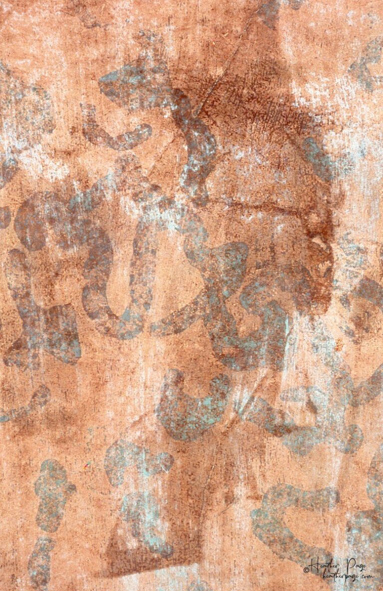 Detail of the back of Con Brio by Heather Page, a 61.5” by 26” relief print on paper of verdigris calligraphic marks dancing over a copper-gilded backdrop