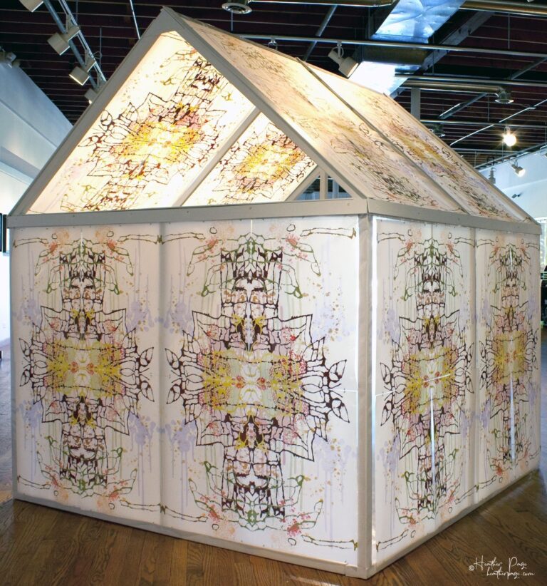 Back view of Daily Dose Installation by Heather Page, an art installation of a 7' by 6' by 6' peaked house frame covered in colorful abstract silkscreen prints