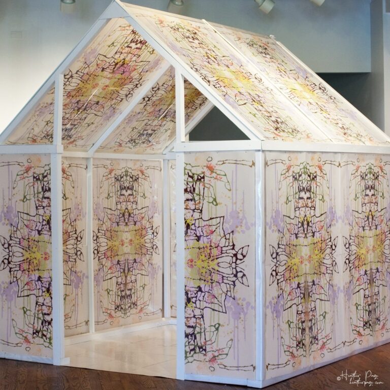 Front view of Daily Dose Installation by Heather Page, an art installation of a 7' x 6' x 6' peaked house frame covered in colorful abstract silkscreen prints