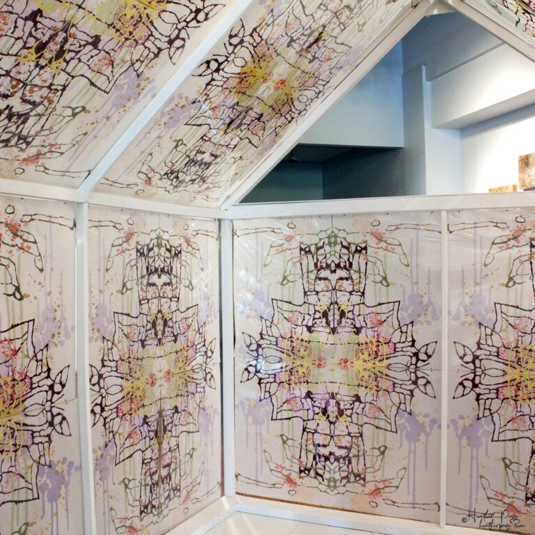 Interior of Daily Dose Installation by Heather Page, an art installation of a 7' by 6' by 6' peaked house frame covered in colorful abstract silkscreen prints