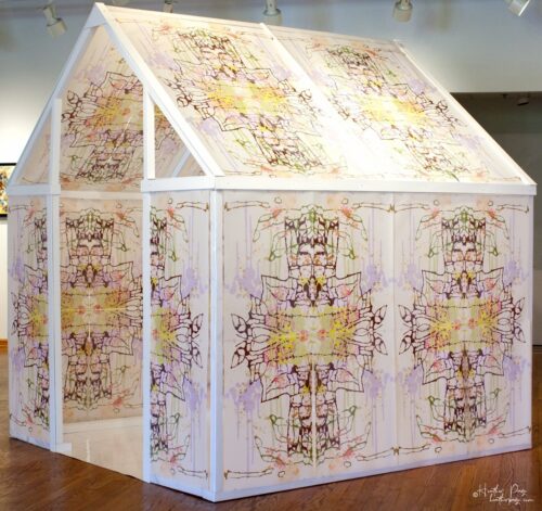 Side view of Daily Dose Installation by Heather Page, an art installation of a 7' x 6' x 6' peaked house frame covered in colorful abstract silkscreen prints
