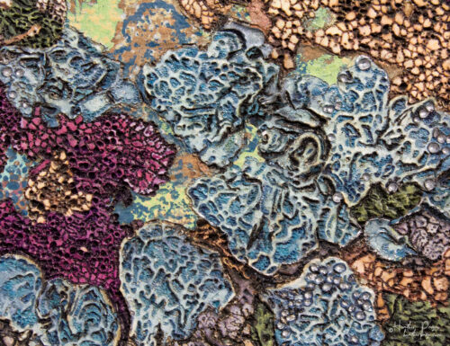 Detail of La Tempête by Heather Page, a 20” by 26” by 2” silkscreen, painting, woodburning, & collage on panel of a cluster of blue lichens on a copper ground
