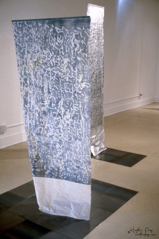 Back view of Rondo by Heather Page, a 74” by 38” relief print, rubbing, and drawing on paper of calligraphic marks looping over a dappled silver ground